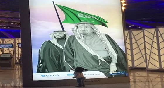 عفوية وبراءة.. طفلة تمد يدها لمصافحة صورة خادم الحرمين الشريفين